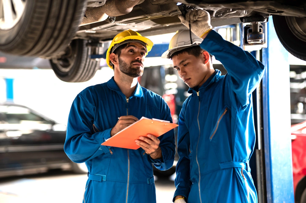 Two professional look technician inspecting car underbody and suspension system by using check list in modern car service shop