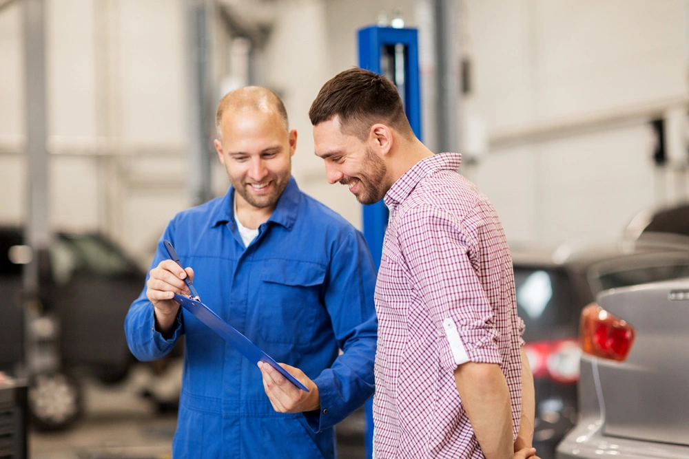 mechanic with clipboard talking to man or owner at car shop